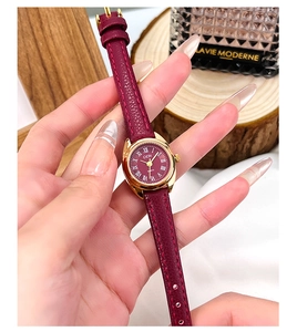 Détail d'une montre rétro en cuir rouge avec cadran doré et chiffres romains sur un plateau