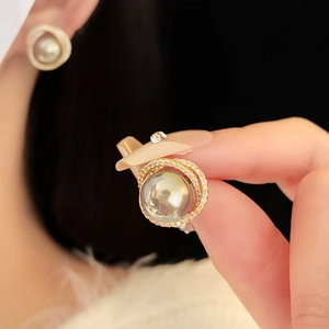 Macro shot of gold hollow earrings featuring a green pearl surrounded by zircon crystals