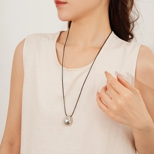 Pendentif ovale argenté minimaliste sur cordon noir porté sur un haut en lin