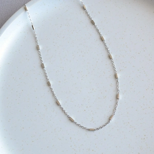 Close-up of minimalist silver chain necklace with small square beads on a white tray
