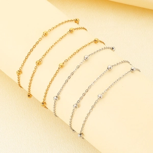 Detail view of layered gold and silver bead chain bracelets with smooth metallic finish