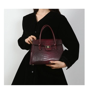 Detail of burgundy crocodile-embossed tote bag featuring a gold twist lock and handle