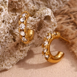 Macro shot of 18K gold plated C-shaped earrings with zircon on natural stone