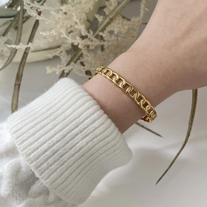Close-up of golden chain bracelet worn over a white sweater with elegant floral accents