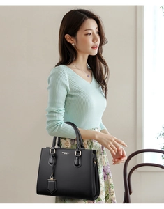Detail of a black textured leather handbag with gold hardware held by a fashion model