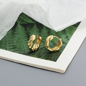 Macro detail of golden twisted rope metal hoop earrings on a decorative plant card