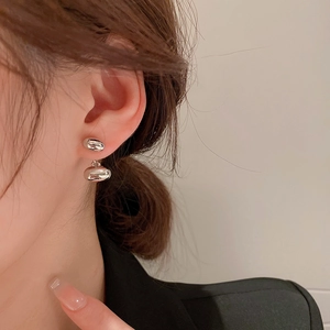 Close-up of elegant silver double bean-shaped drop earrings on model in warm indoor setting