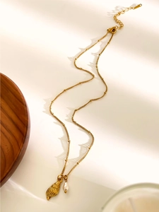 Close-up of golden conch shell pendant with white pearl on a titanium steel necklace