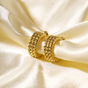 Detailed close-up of golden braided hoop earrings on elegant silk background
