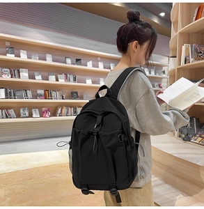 Seitenansicht eines schwarzen Rucksacks mit Seitentaschen, von einem Modell in einer Bibliothek
