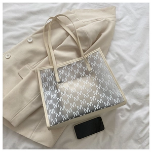 Detail of transparent large capacity tote bag with white M letter print and cream trim