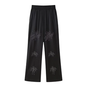 Detail of black satin wide-leg pants with shimmering rhinestone floral embroidery