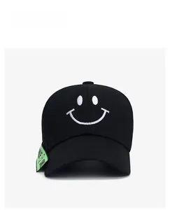 Detail of a black baseball cap with white smiley face embroidery and a green ribbon tag