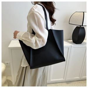 Minimalist black oversized tote bag shown on model shoulder for commuter style