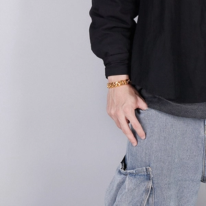 Close-up of a gold Cuban link bracelet on a wrist against a neutral streetwear background