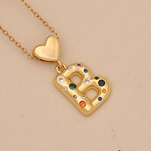 Close-up of golden heart pendant with a colorful zircon letter B on a beige background