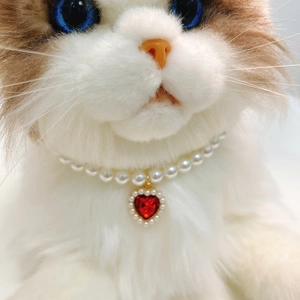 Detail of pet pearl necklace with red heart crystal pendant on a white cat