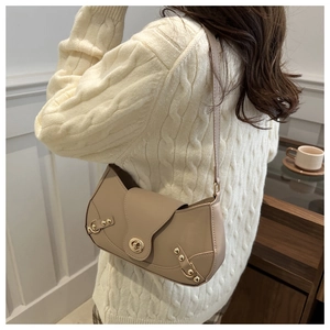 Detail view of beige saddle bag with gold rivets and flip-lock on a knit sweater