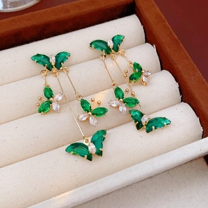 Détail de boucles d'oreilles pendantes dorées avec papillons en zircons verts et clairs