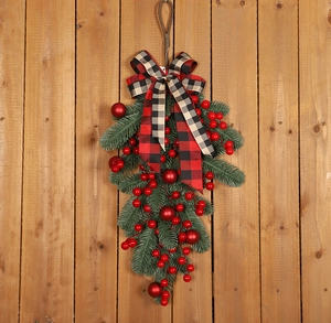 Close-up of Christmas pine teardrop swag with red berries and plaid bow on wood background