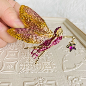 Detailed close-up of a fairy brooch with purple enamel wings and a shiny star charm
