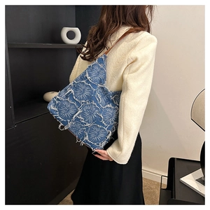 Detail of blue denim tote bag with white fringed floral patterns and brown shoulder strap