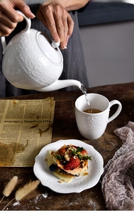 Detail view of embossed white ceramic tea set with pot and cup on a vintage wood table