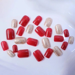 Detail of short square press-on nails in glossy red and champagne gold glitter finish