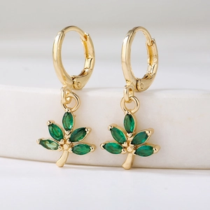 Elegant gold earrings with leaf pendants and green marquise zircons on white surface