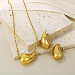 Détail d'une parure dorée en gouttes d'eau avec chaîne à billes sur blocs de pierre beige