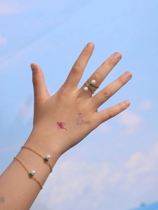 Golden crown ring and bracelet with pearl and green leaf details on hand outdoors