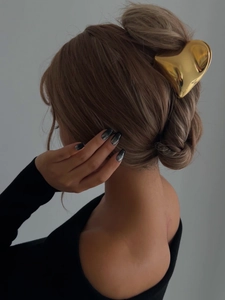 Detailed side view of a gold heart-shaped metal hair claw clip worn in a messy bun hairstyle