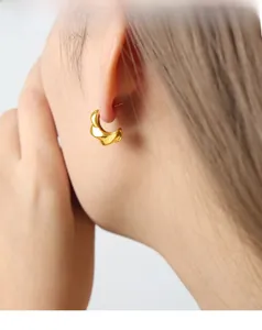 Detail view of gold-plated twisted hoop earring with polished metallic texture on ear