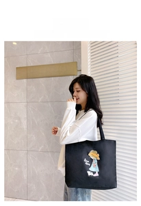 Outdoor shot of a black canvas tote bag with a cartoon girl illustration and Nice Day text