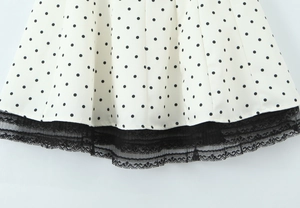 Detail of white dress with black polka dots and delicate black lace trim at the hemline