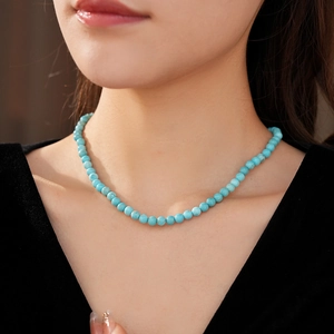 Detail of turquoise beaded necklace on model neck highlighting vivid blue round beads