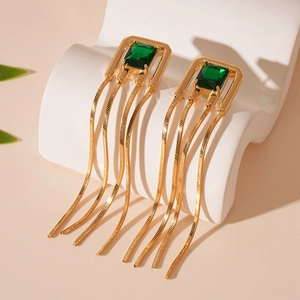 Macro shot of gold tassel earrings with square green gemstone on white marble display