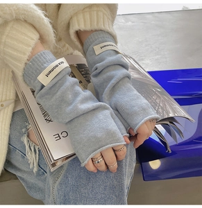 Close-up of light blue knitted fingerless gloves with a white nice moment tag on hand