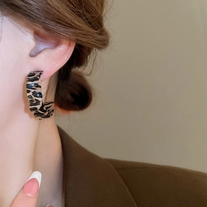 Close-up of leopard print C-shape earrings worn by a model in a brown blazer jacket