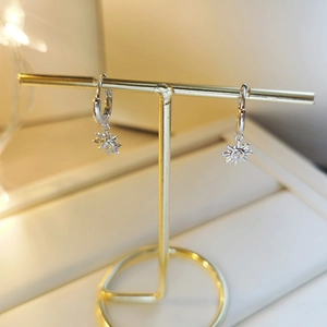 Macro detail of silver sun charm earrings with zircon inlay on a golden jewelry display stand