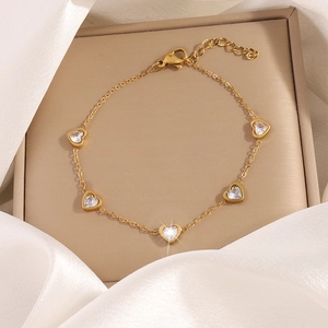 Dettaglio macro del bracciale dorato con zirconi a cuore e chiusura a moschettone
