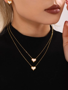 Detailed view of model wearing gold double-layer necklace and matching heart stud earrings