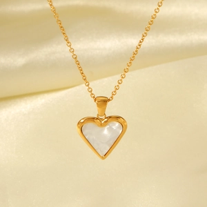 Detail of a gold heart pendant necklace with white mother-of-pearl on champagne silk