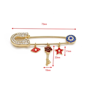 Detailed view of gold safety pin brooch with blue evil eye and rose key charms, 73mm length