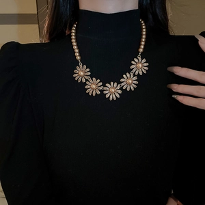 Detail of vintage gold flower necklace with pearls worn on black turtleneck sweater
