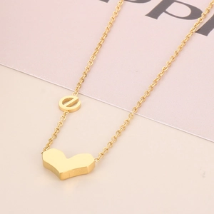 Collier en acier titane doré avec pendentif cœur 3D sur un fond rose délicat