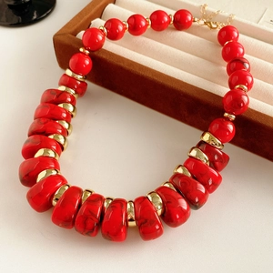 Détail de perles rouges texturées marbre et d'entretoises dorées sur un collier vintage