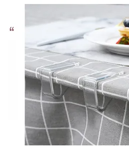 Close-up of transparent U-shaped tablecloth clips securing grey checkered fabric on a table