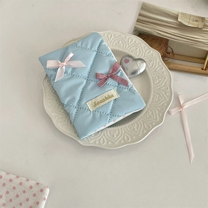 Close-up of a light blue quilted passport holder featuring a pink ribbon bow and Sozakka tag