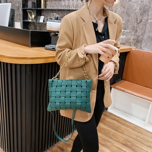 Modern dark green woven handbag with chunky gold chain strap in a cafe setting